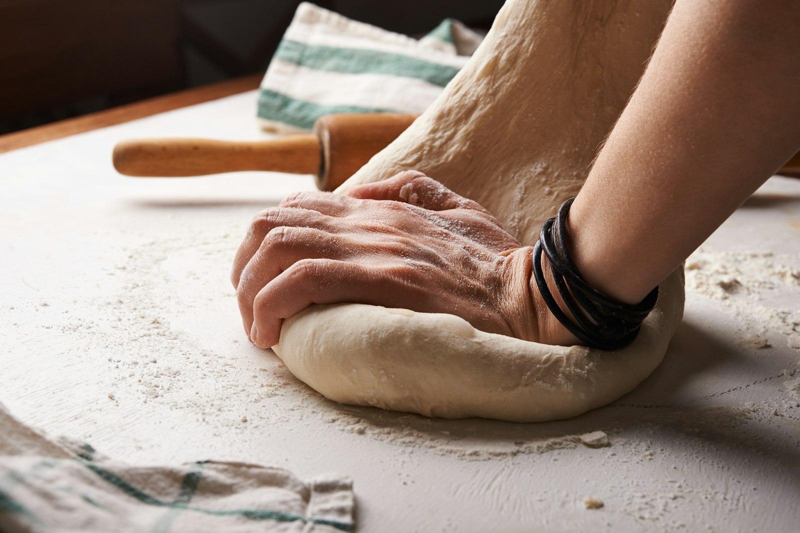 Hands shaping dough beside a wooden rolling pin